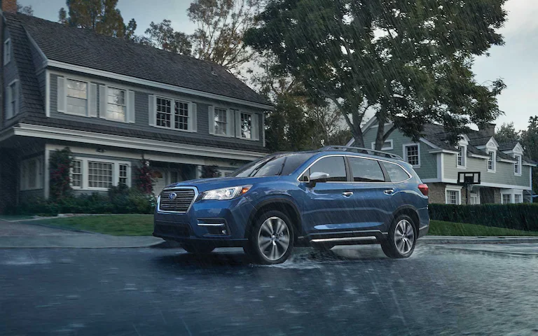 A Subaru Ascent driving in the rain through a neighborhood.