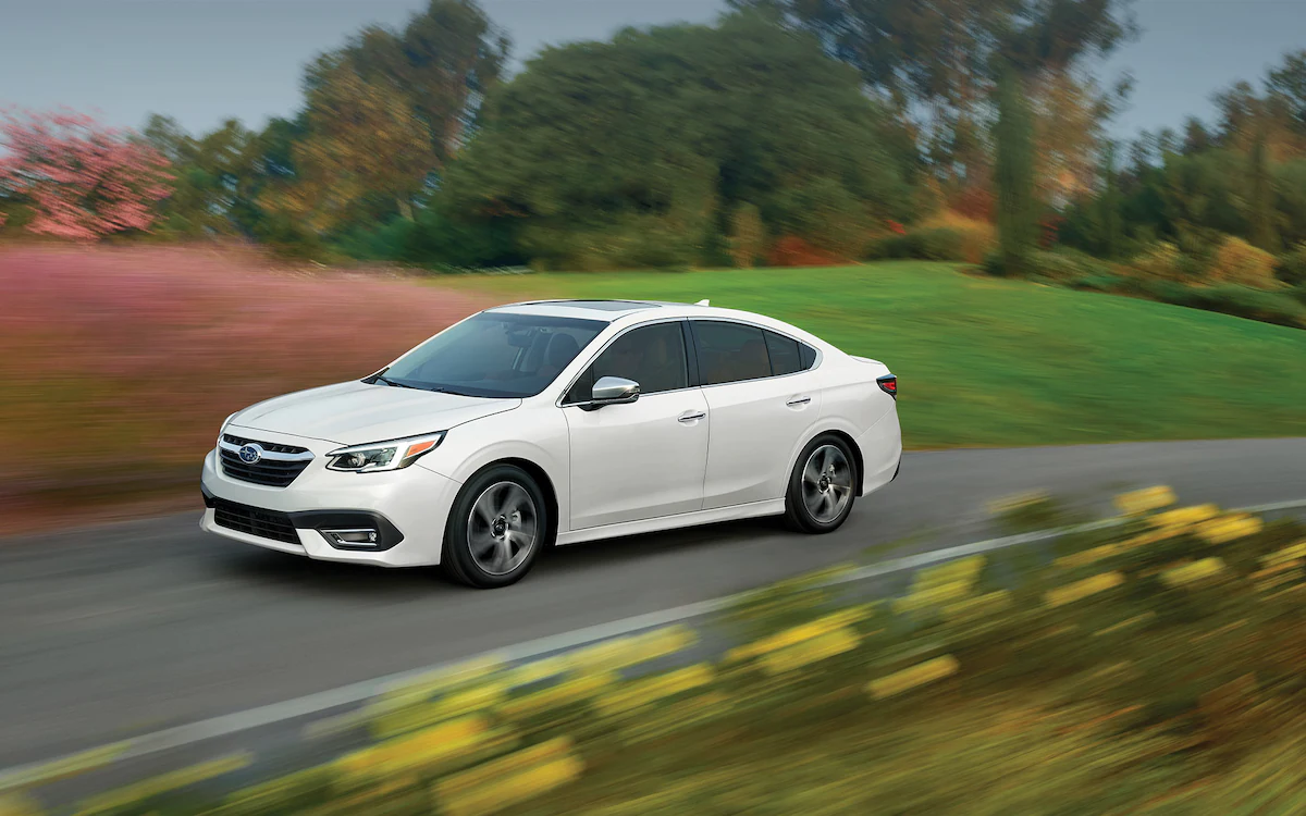 2022 Subaru Legacy driving on road with Surfboard on roof rack.